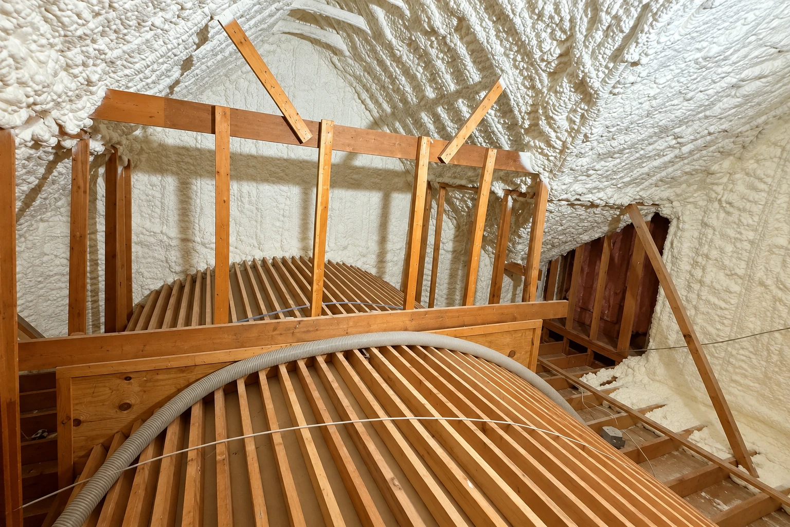 An attic with exposed wooden framing and thick white spray foam coating the roof and walls.