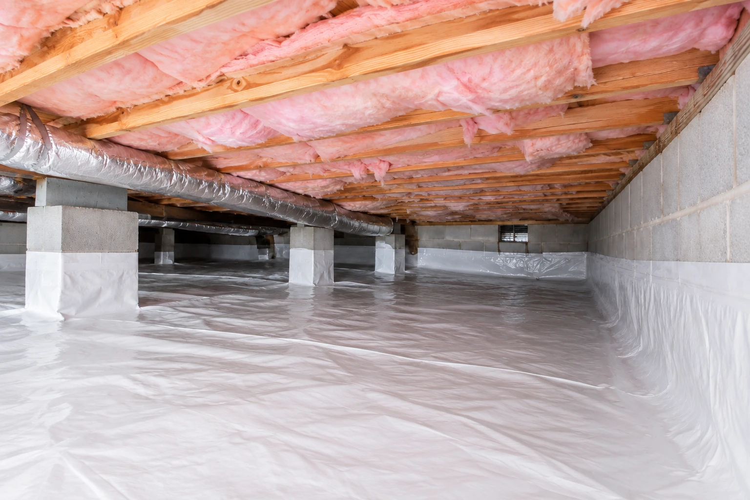 A crawl space has pink insulation between ceiling joists and a white vapor barrier covering the floor and lower supports.